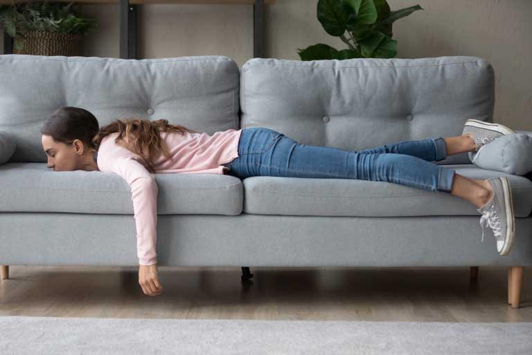 Young woman lying buried her face in sofa feels tired X115®